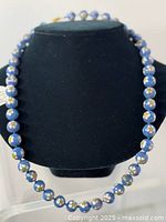 Full view of the necklace on display showing the knotted blue enamel beads with floral designs.