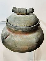 Front diagonal view of vintage Raku pottery bowl with lid on white surface highlighting textured earthy colors and ribbed handle detail