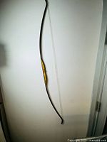 Side view of the full bow showing the wooden body and black edging, hung on a white wall.