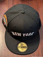 Front view of black fitted baseball cap showing New York embroidered text and size sticker on brim.