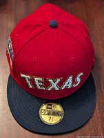 Front view of Texas Rangers baseball cap with red crown, navy visor, and 'TEXAS' embroidered on front.