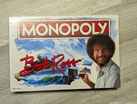 Top view showing the Bob Ross Monopoly game sealed box front with Bob Ross image and title.