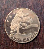 Front side of bronze coin showing stylized hands with year 1920 and 'GROUP OF SEVEN' inscription.