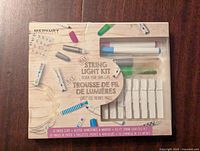 Front of the Merkury String Light Kit box showing contents including photo clips, markers, and string lights.
