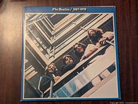 Front cover of first Beatles 1967-1970 vinyl record showing four band members looking down from a balcony, colorful attire.
