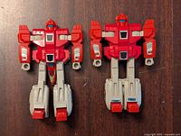 Front view of two red and gray G1 Transformer Autobot clone figures on dark wood surface