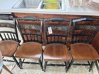 Front view of four Hitchcock chairs arranged side by side showing floral decoration and wooden seats