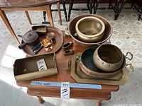 Overview photo of the copper and metal items arranged on a wooden side table showing various trays, bowls, teapot, and container.