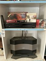 Bose Acoustic Wave Music System on bottom shelf with Nakamichi 5-disc CD changer placed on shelf above, surrounded by CD cases for classical music, Van Morrison, and others. Both systems include remotes, visible.