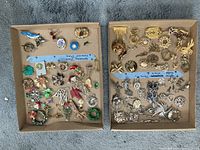 Two trays of assorted gold and silver plated brooches and holiday pins arranged loosely.