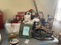 Wide view of the lot showing Christmas figurines, a decorative picture frame, Mikasa bowls, and other assorted holiday items including wrapping paper and cards.