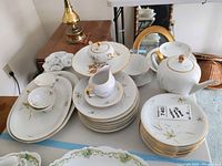 Full view of large oval platter, cups, saucers, teapot, sugar bowl, creamer, and stack of plates with gold trim and floral decoration.