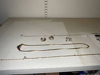 Overview of three necklaces and two pairs of earrings laid out on white shelf