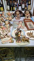 Overview of multiple Hummel figurines, plates, framed prints and collector’s book arranged on table