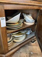Wooden cabinet shelf with assorted plates, bowls, and serving platters stacked inside