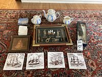 Full lot layout showing all items on a carpet including the Mayflower teapot set, framed quill set, copper sailboat, framed ship print, and four Mayflower trivets.