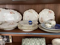 Shelf display of Triumph Limoges plates, trays, and decorative eggs with gold rims and floral accents.