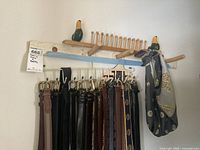 Wooden tie rack with multiple pegs, decorated with two painted duck heads, holding several men's belts in black, brown, and dark tones, plus some ties