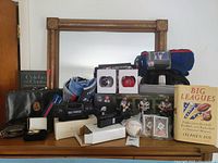 Wide front view of the lot displayed on dresser showing Patriots figurines, blankets, Babe Ruth baseball, sports cards, mini radio, reading light, Edifier speaker, thermos set, Barlow clip, and book.