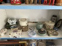 Shelf display of assorted pill boxes and trinket holders showing a variety of shapes, styles and floral or nature themes