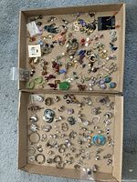 Top view of two cardboard trays filled with many pairs of earrings including different metals and colors, showing the variety of shapes and styles.