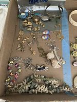 Photo of a box with a collection of mixed jewelry including earrings shaped like fish, birds, shells, and circular pendants.