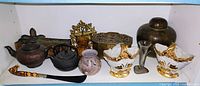 Shelf with various items including the cloisonne ginger jar, teapots, brass box, vases, glass vase and horseshoe horn item all shown.
