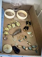 Overview of carved bangles, face charms, black tube bracelet, silver fish and various stone pendants in box