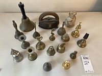 Overview of the 18 vintage bells including a large bell with black handle and various smaller brass and bronze bells of different decorative styles and sizes.