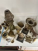 Full view of all brass and copper decorative items on a white surface, showing the variety of cat statues, dolphin, boat, shells, candle sticks, and ashtray.
