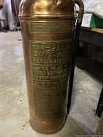 Full view of the copper fire extinguisher showing the brass label with manufacturer and usage instructions.