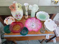 Photo of vintage glass bowls and vases arranged on a wooden table, showing different colors, styles, and some chips.