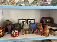 Shelf with assorted vintage figurines including wooden camels and Dala horses, ceramic vases, brass pot, framed silhouettes, lacquered box