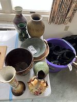 Overview of multiple vintage pottery and ceramic items arranged on a table near a window, showing various vases and bowls of varying shapes and sizes.