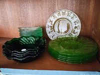 Various colored glass bowls including dark green scalloped-edge bowls and light green embossed bowls beside uranium glass plates.