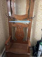 Full view of the front of the wooden hall tree showing the arched mirror, carved backrest, armrests, seat, and metal hooks on sides.