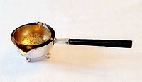 Side angle view showing the hammered silverplate bowl with gold-tone perforated sieve inside, three ball feet, and long black handle.