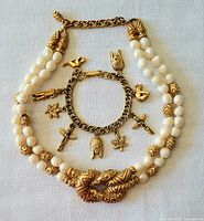 Full view of the chunky faux pearl necklace with textured gold-tone accents and gold charm bracelet with several detailed charms arranged inside the necklace loop.