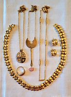 Top-down view of the eight-piece collection laid flat on a white cloth, showing the assorted gold tone costume jewelry items including necklaces, earrings, and ring.