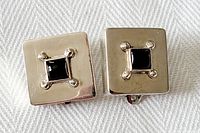 Front view of a pair of square sterling silver clip-on earrings each featuring a square garnet gemstone at the center with four bead prongs.