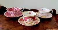 Photo showing three vintage teacup and saucer sets with distinct pink and gold floral patterns on a wooden surface.