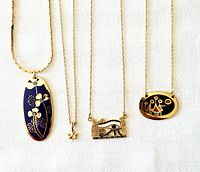 Four signed gold tone chain necklaces with different artistic pendants displayed on white fabric