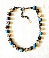 Full view of the necklace showing the blue glass cabochons, grey rivoli beads, and clear faceted crystals arranged on a dark metal chain with clasp and extender.