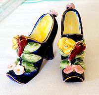 Pair of small vintage porcelain shoes shown from the front with floral decoration visible.