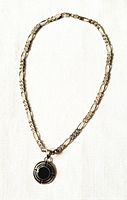 Front view of sterling silver chain necklace with round black onyx pendant on white textured surface.