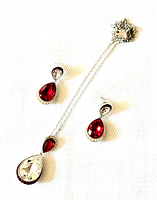 Pair of Swarovski red and clear crystal dangle earrings along with matching pendant necklace chain laid out to display details