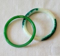 Two jade bangles side by side, one fully green and the other white with green patches.