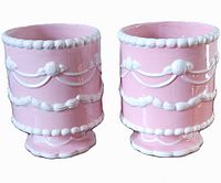 Front side view of two identical pink ceramic pots with white decorative raised pattern and scalloped edges