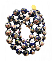Top-down photo showing full coiled necklace with graduated bead sizes and floral cloisonne enamel on cobalt blue background.