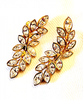 Pair of gold-tone clip-on earrings featuring multiple clear crystals arranged as leaves on a branch, displayed on light fabric.